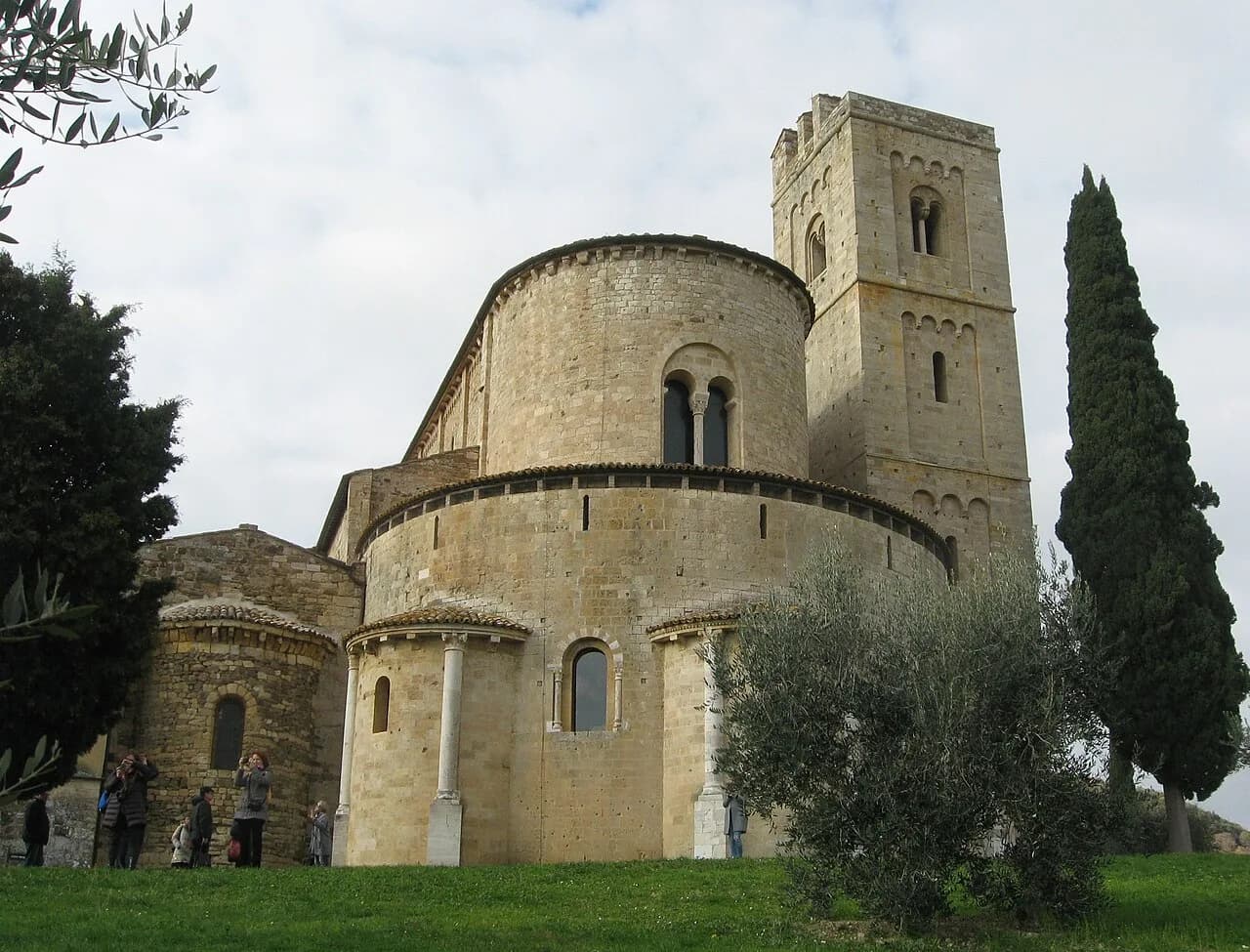 Rounded stone apses and the bell tower of Sant’Antimo Abbey beside a tall cypress tree